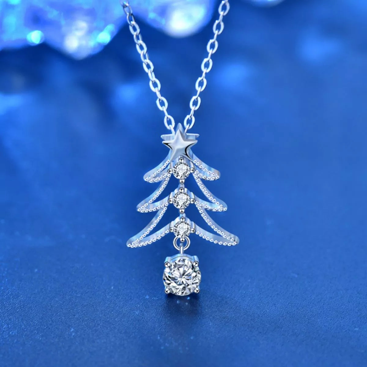 Silver Christmas tree necklace with star and ball pendant on a blue background