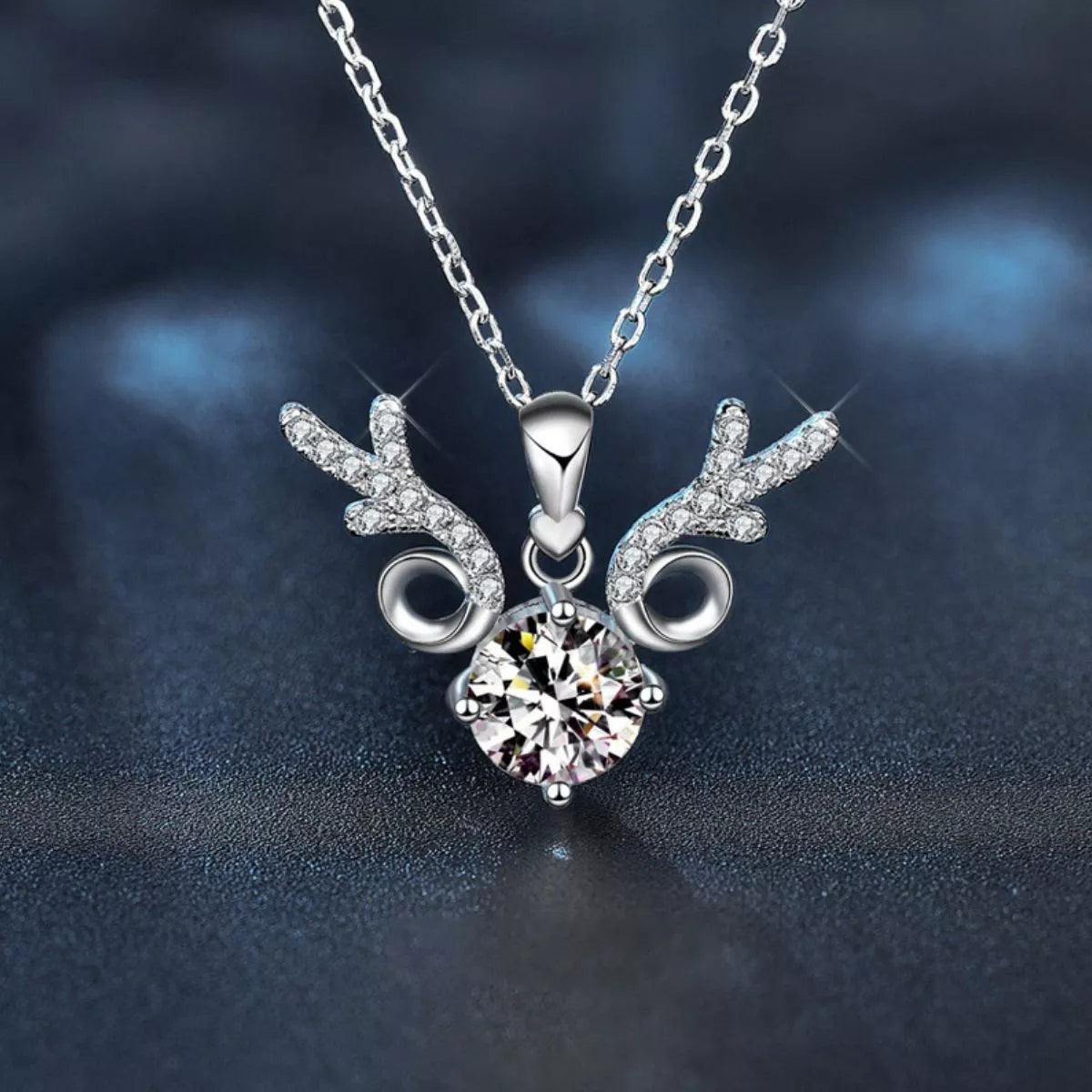 Silver deer head necklace with a heart-shaped gem on a dark background