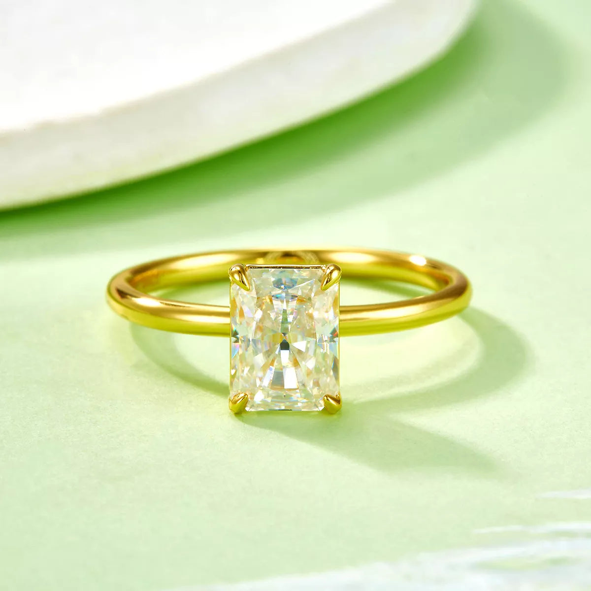 Gold ring with a rectangular diamond on a light green surface